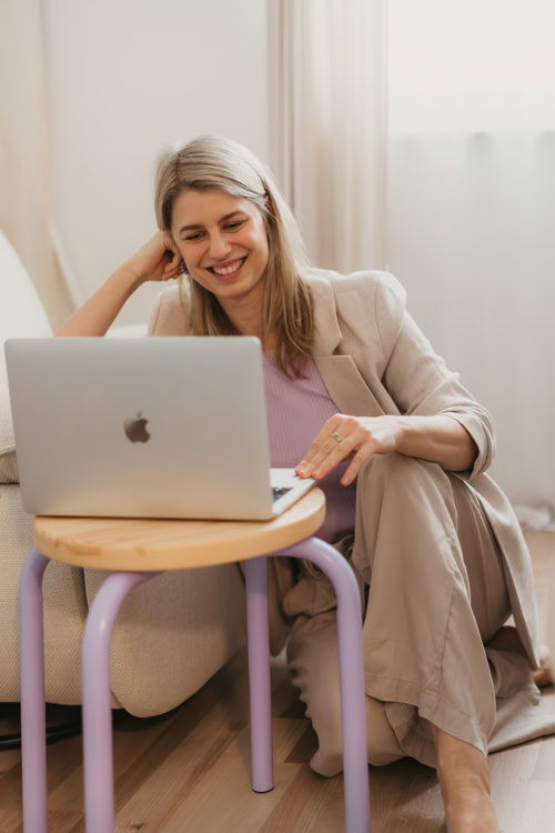 Wordpress-Webdesignerin Finja sitzt auf dem Fußboden hinter einem lilafarbenen Hocker und schaut auf ihren Laptop.